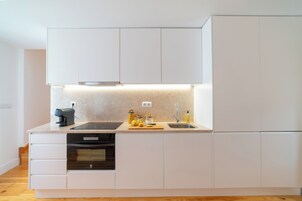 Una cocina moderna con armarios blancos, horno empotrado, cafetera y tabla de cortar con limones.