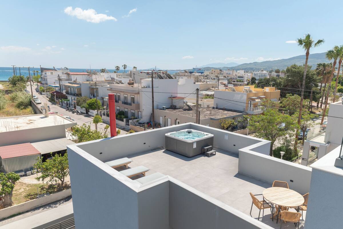 Terraço com banheira de hidromassagem, área de estar externa e vista para o mar e prédios.