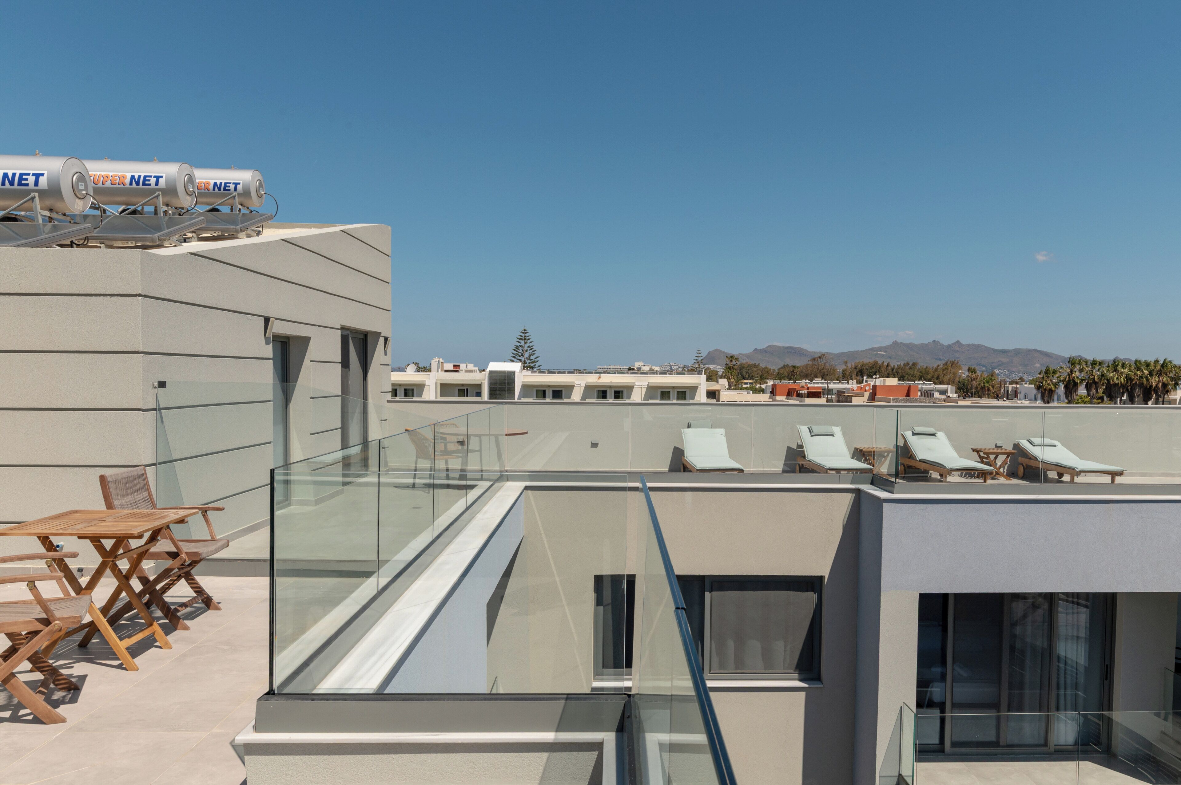 A rooftop terrace with glass railings, lounge chairs, and a solar panel array.