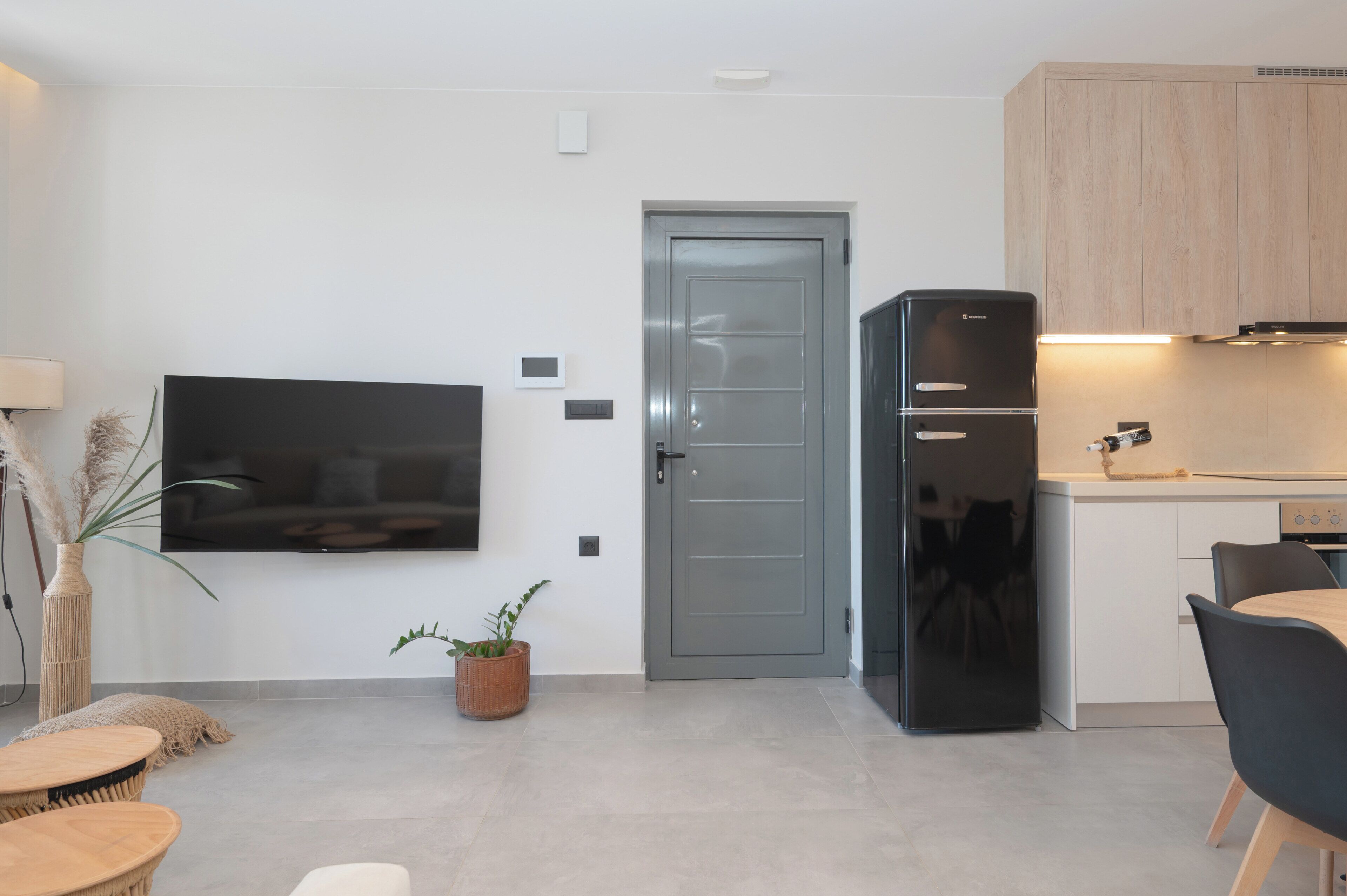 A modern kitchen with a built-in refrigerator, a flat-screen TV mounted on the wall, and a dining area with a table and chairs.