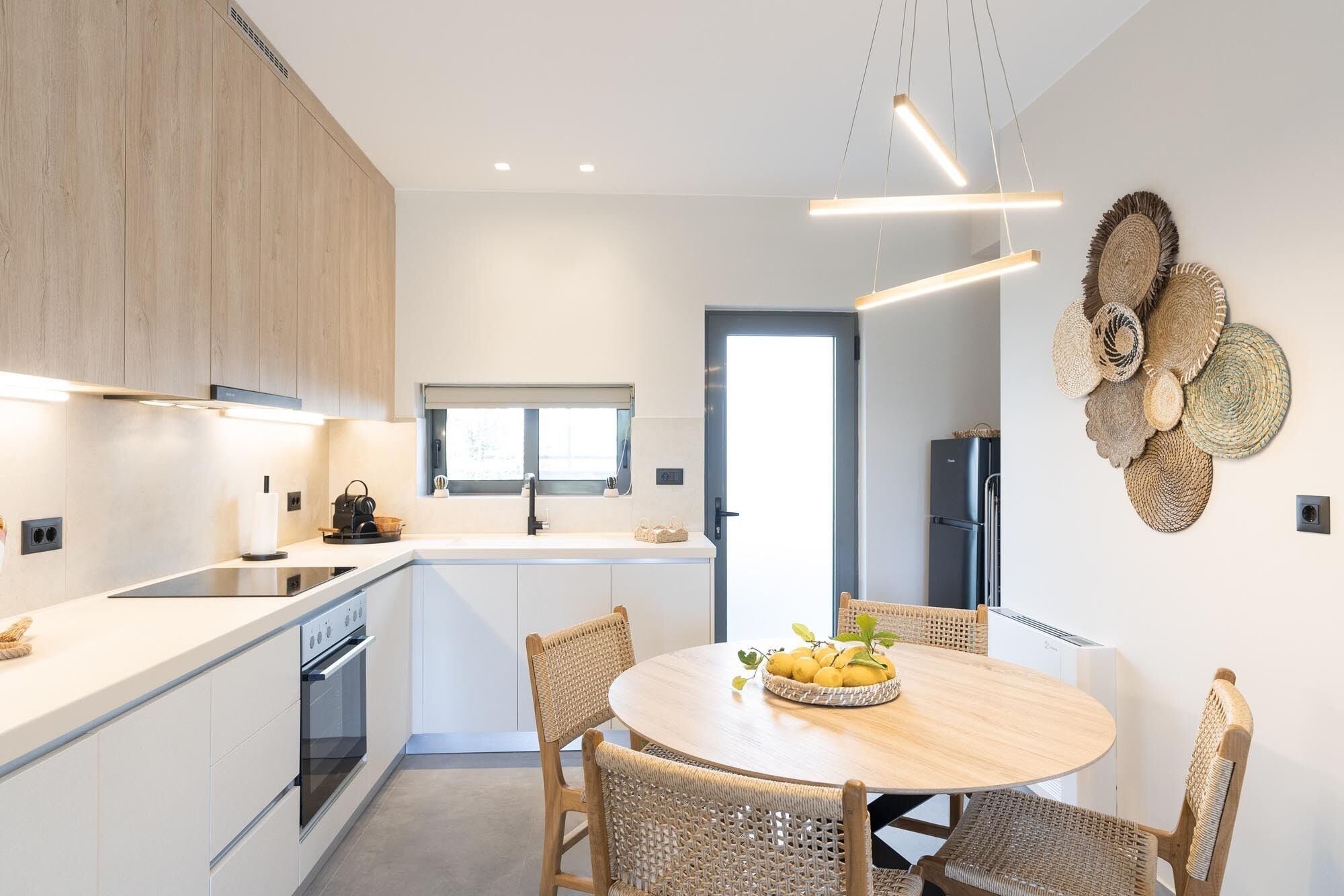 Une cuisine moderne dotée d’un îlot central, d’appareils électroménagers intégrés et d’un coin repas avec des chaises en osier.
