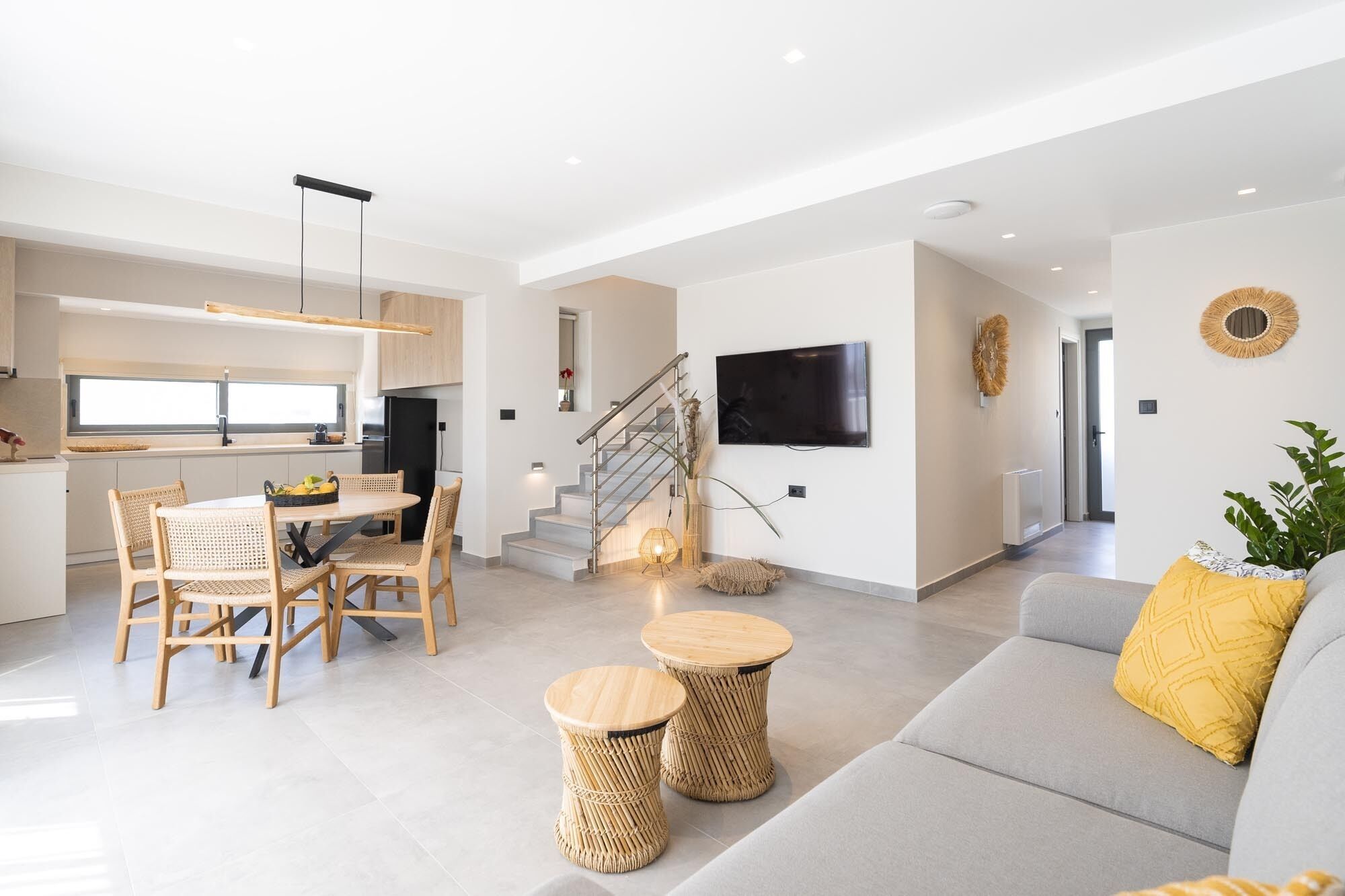 A modern living space with a kitchen, dining area, and a staircase leading to another level.