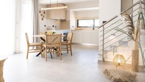 Eine moderne Küche mit weißen Schränken, ein Essbereich mit Korbstühlen und eine Treppe mit Geländer.