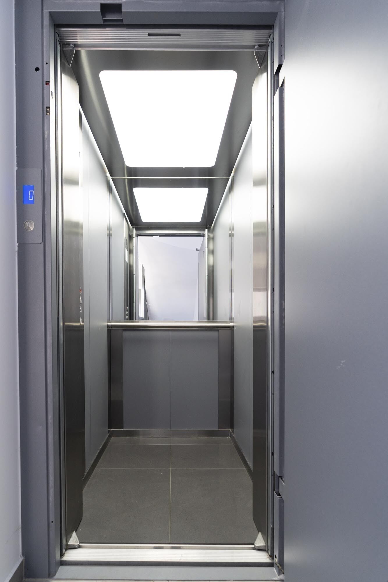 An empty elevator with a modern design, featuring a metallic finish and a clear ceiling.