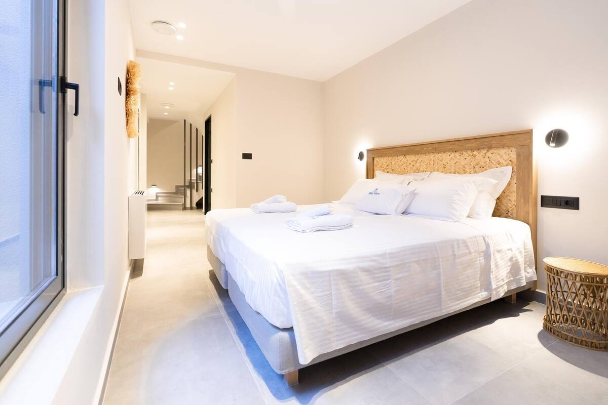Quarto de hotel moderno com uma cama grande, cabeceira de madeira e mesa de cabeceira de vime.