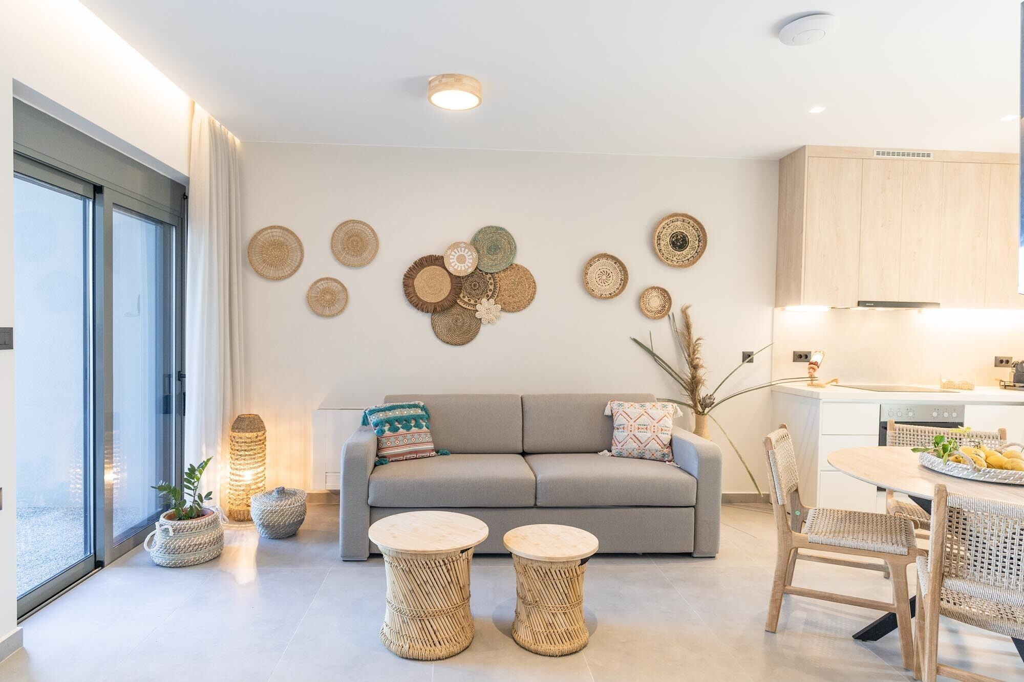 A modern living room with a grey sofa, two round wicker coffee tables, and a dining area with a wooden table and chairs.