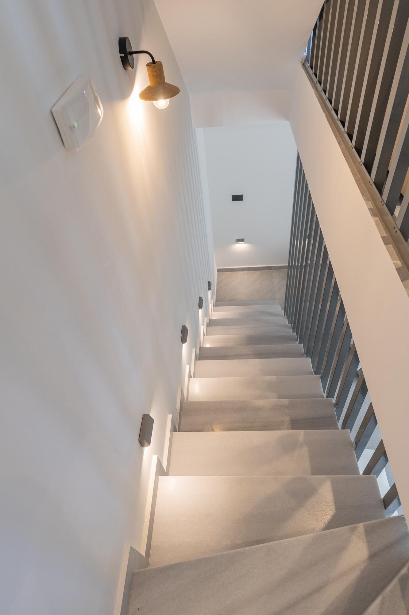A modern staircase with a minimalist design, featuring a light-colored floor and a railing with vertical slats.