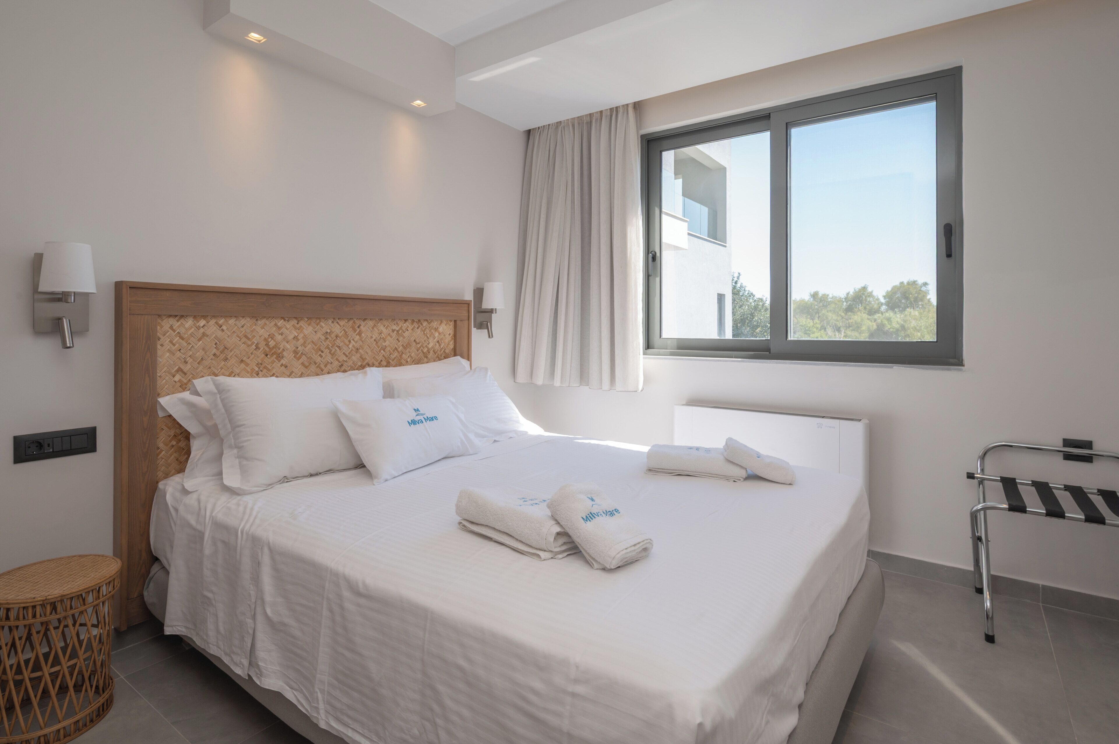 Une chambre d’hôtel moderne avec un grand lit, deux tables de chevet, une fenêtre avec des rideaux et une vue sur l’extérieur.