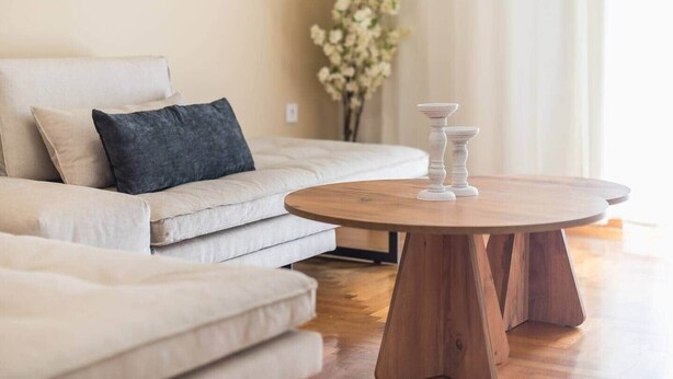 A modern living room with a beige sofa, a round wooden coffee table, and a vase with white flowers. - Athena House Elegant Stay  By Greece Apartments (Vyronas)