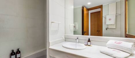 A modern bathroom with a white sink, mirror, and two bottles of toiletries on the counter.