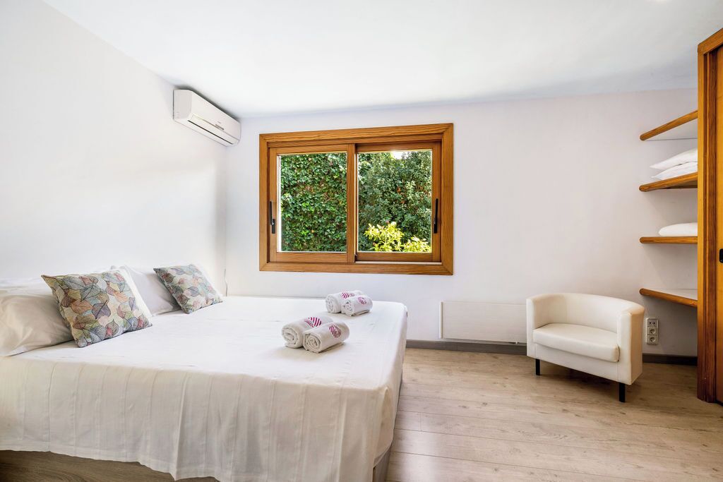 A bedroom with a bed, pillows, a chair, a window, and a shelf.