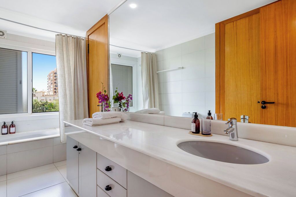 Un baño moderno con un espejo grande, lavamanos doble y una bañera.
