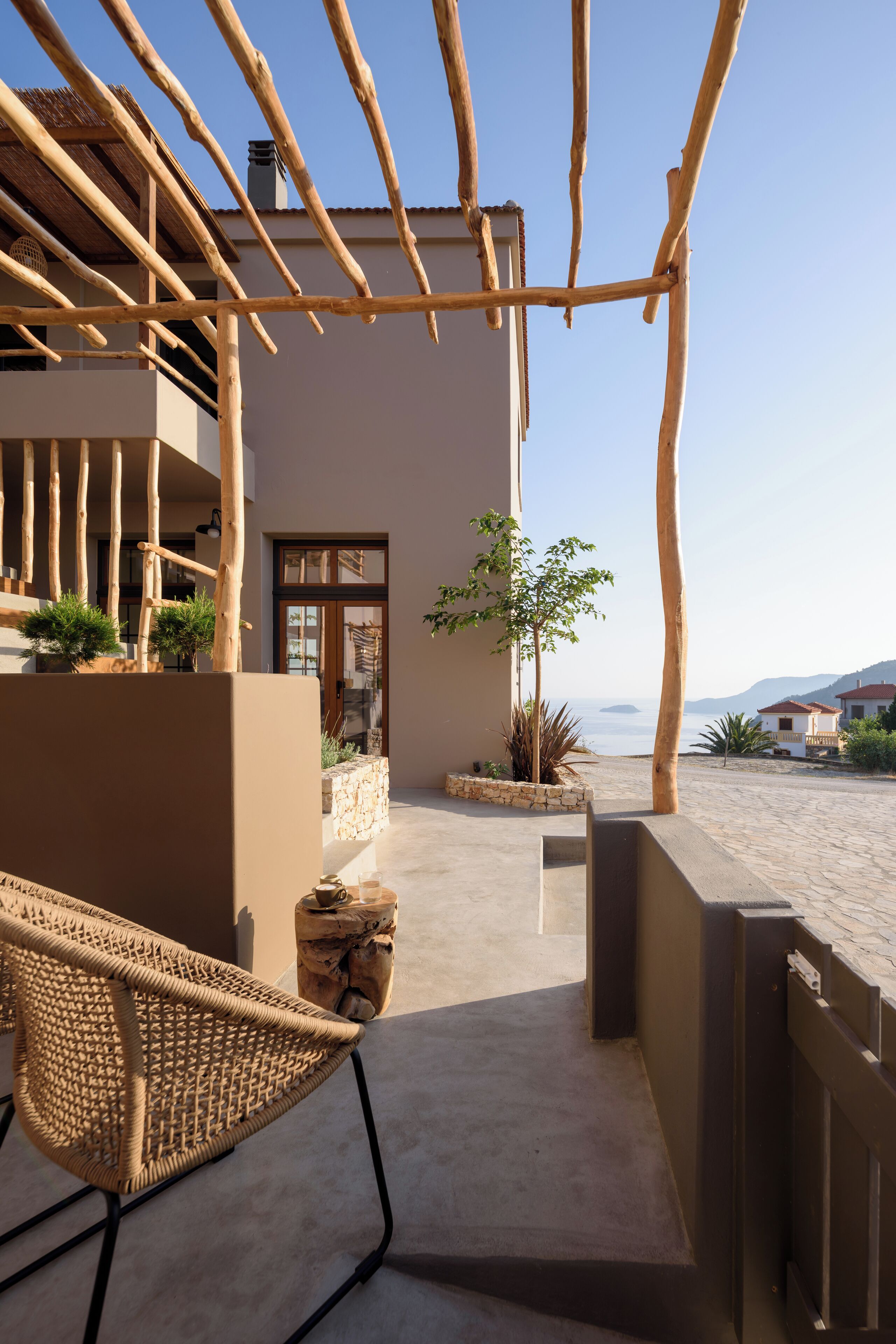 A modern outdoor area with a wicker chair, a stone planter, and a view of the sea.