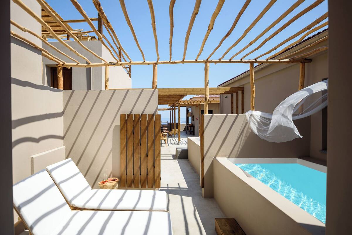 A sunlit outdoor area with a pool, wooden pergola, and lounge chairs.