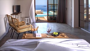 A bedroom with a bed, a wooden coffee table with a book, glasses, and grapes, a wicker chair, a small stool, and a TV. - Aletri Swim Up Boutique Hotel (Alonissos)