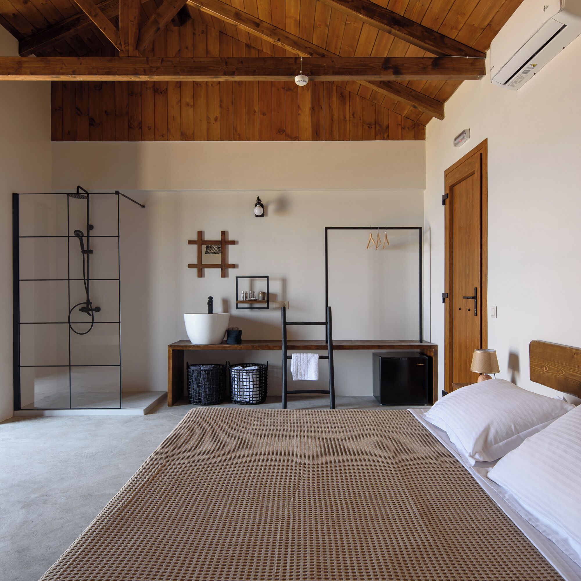 Un dormitorio con una cama, un armario de madera, un escritorio con una silla, un refrigerador negro pequeño y una lámpara colgante.