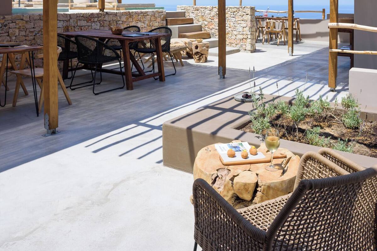 An outdoor patio with wooden pergolas, stone walls, and a view of the sea.
