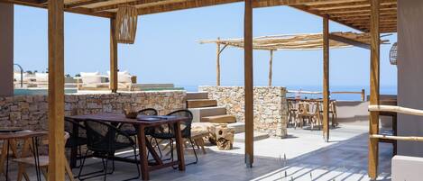 Un patio exterior con pérgolas de madera, muros de piedra y vista al mar.