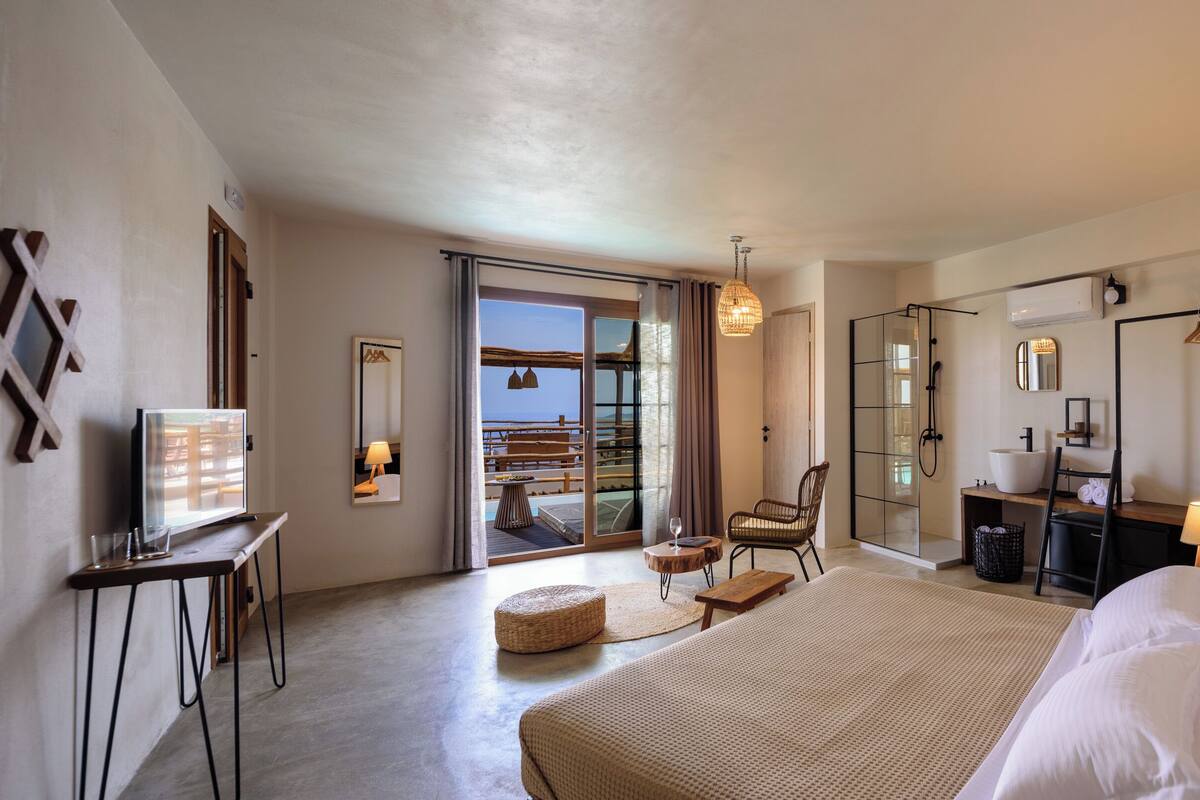 A hotel room with a large bed, a desk with a computer, a chair, a small table, a sink, and a shower.