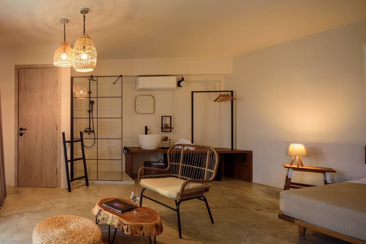 A cozy room with a bed, a wicker chair, a small table with a glass, and a hanging light fixture.
