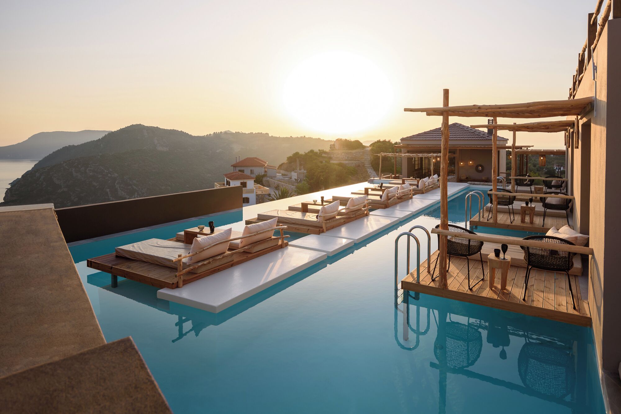 Piscina infinita en la azotea con sillones de descanso y vistas al mar y las colinas.