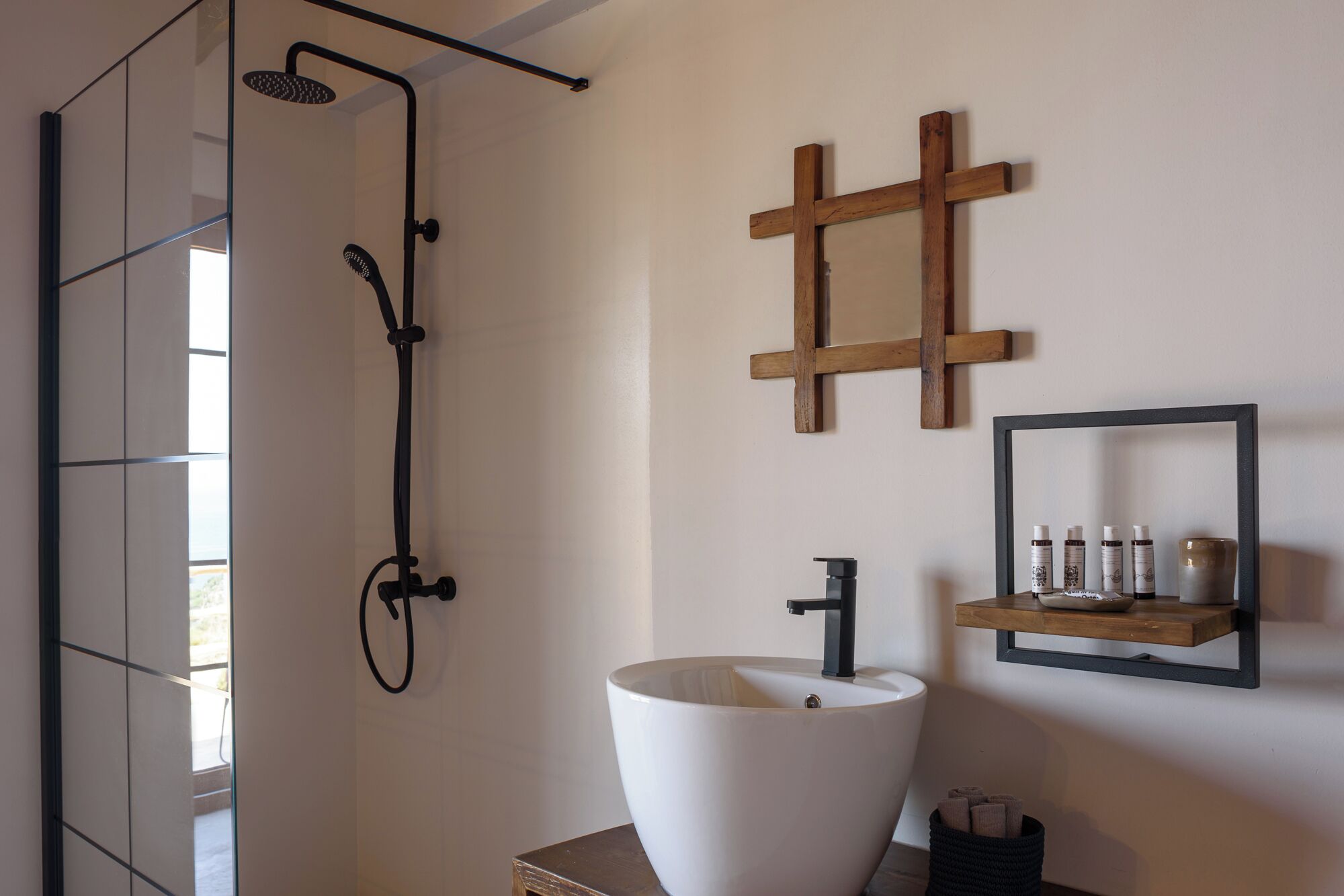 A modern bathroom with a large white sink, a wooden cross, and a shelf with toiletries.