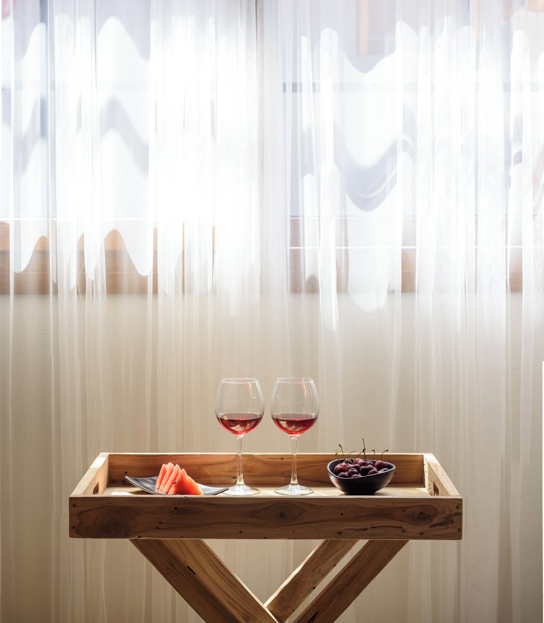 A wooden table with two wine glasses and a bowl of cherries.