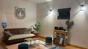 Una sala de estar con un sofá marrón, una mesa de centro, una estantería, una planta en maceta y una obra de arte en la pared.