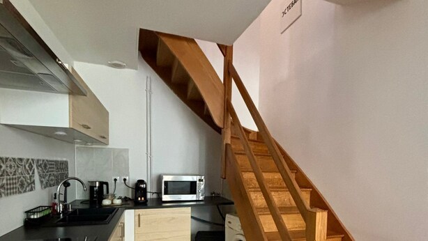 Cocina compacta con escalera de madera, lavadora y microondas.