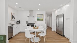 Een moderne keuken met witte kastjes, een roestvrijstalen koelkast en een eethoek met een ronde tafel en witte stoelen.