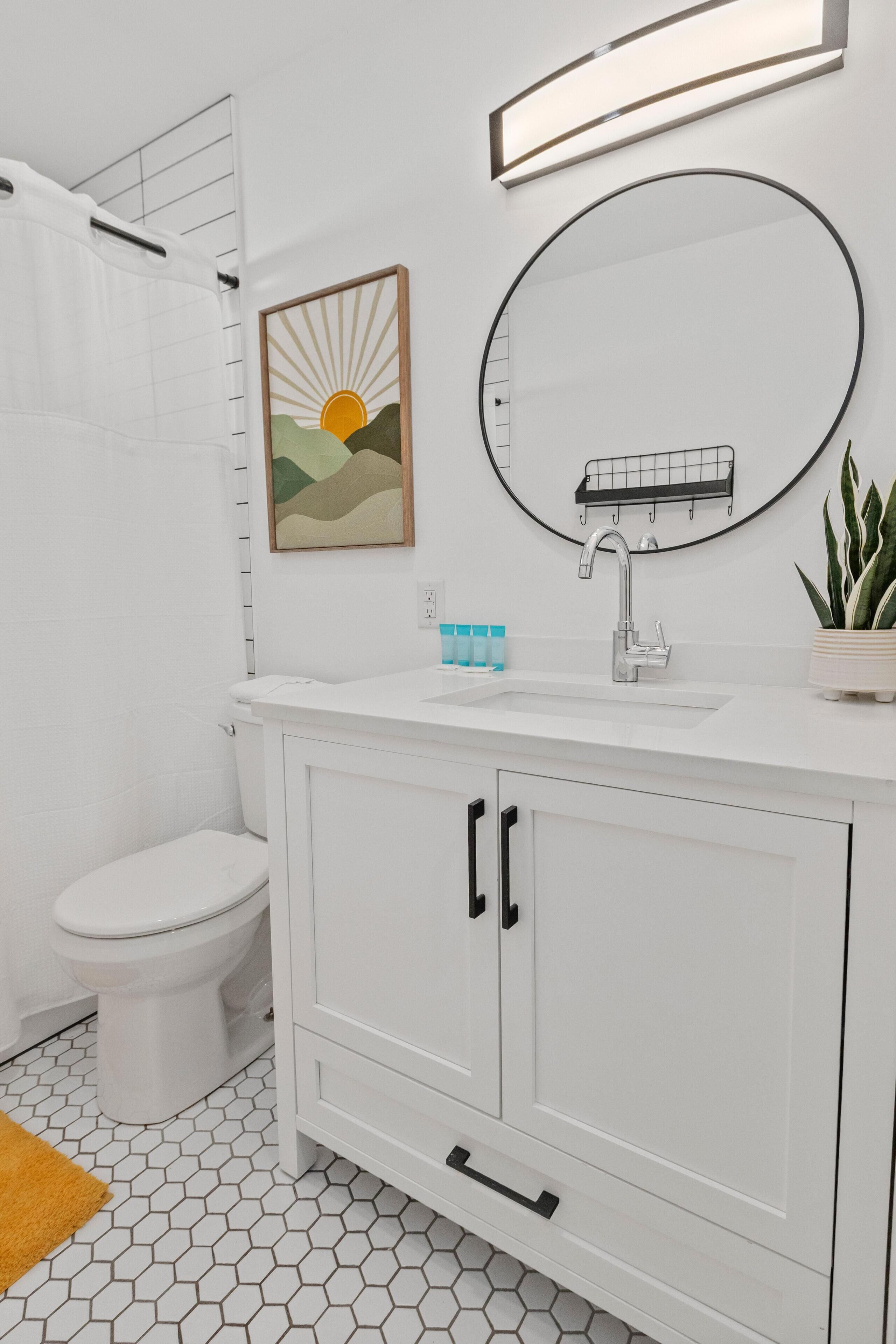 A modern bathroom with a white sink, a mirror, a toilet, and a shower curtain.