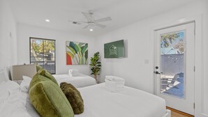 Een hotelkamer met twee bedden, een plafondventilator, een raam met uitzicht en een bord aan de muur.
