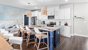 Une cuisine moderne avec des meubles blancs, un îlot central, des tabourets de bar et des luminaires suspendus.
