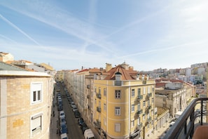 A street view of a city with buildings, cars parked along the street, and a clear sky. - Desterro (Lisbon)