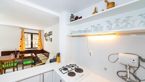 A compact kitchen with a gas stove, a sink, and a dining area with a table and chairs. - Heritage Home Cvita (Murter)