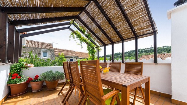 A covered outdoor patio with wooden furniture and potted plants. - Heritage Home Cvita (Murter)