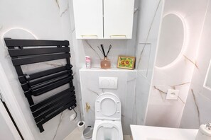 Ein kleines Badezimmer mit einem schwarzen Handtuchhalter, einer Toilette, einem Waschbecken und einem Waschtisch mit Spiegel.