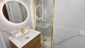A modern bathroom with a white marble vanity, gold fixtures, and a glass-enclosed shower. - Terrace Studio Steps from Trocadéro & Eiffel (Paris)