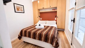 A bedroom with a bed, wooden wardrobe, and a window. - Terrace Studio Steps from Trocadéro & Eiffel (Paris)