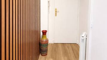 Un couloir avec un mur recouvert de lambris en bois, un vase coloré et une porte blanche.