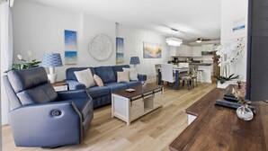 Een moderne woonkamer met een blauwe bank, een houten salontafel en een keuken op de achtergrond.