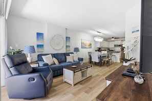 A modern living room with a blue sofa, a wooden coffee table, and a kitchen in the background. - Beautiful Spacious Condo walk to Beach & Coligny- Indoor Outdoor Pool, Hot Tub ! (Hilton Head Island)