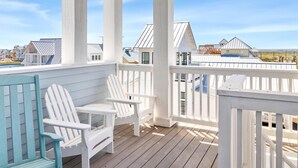 Un porche cubierto con barandillas blancas, dos sillones Adirondack y vistas a casas al fondo.