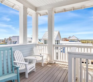 Eine überdachte Veranda mit weißen Geländern, zwei Adirondack-Stühlen und Blick auf Häuser im Hintergrund.