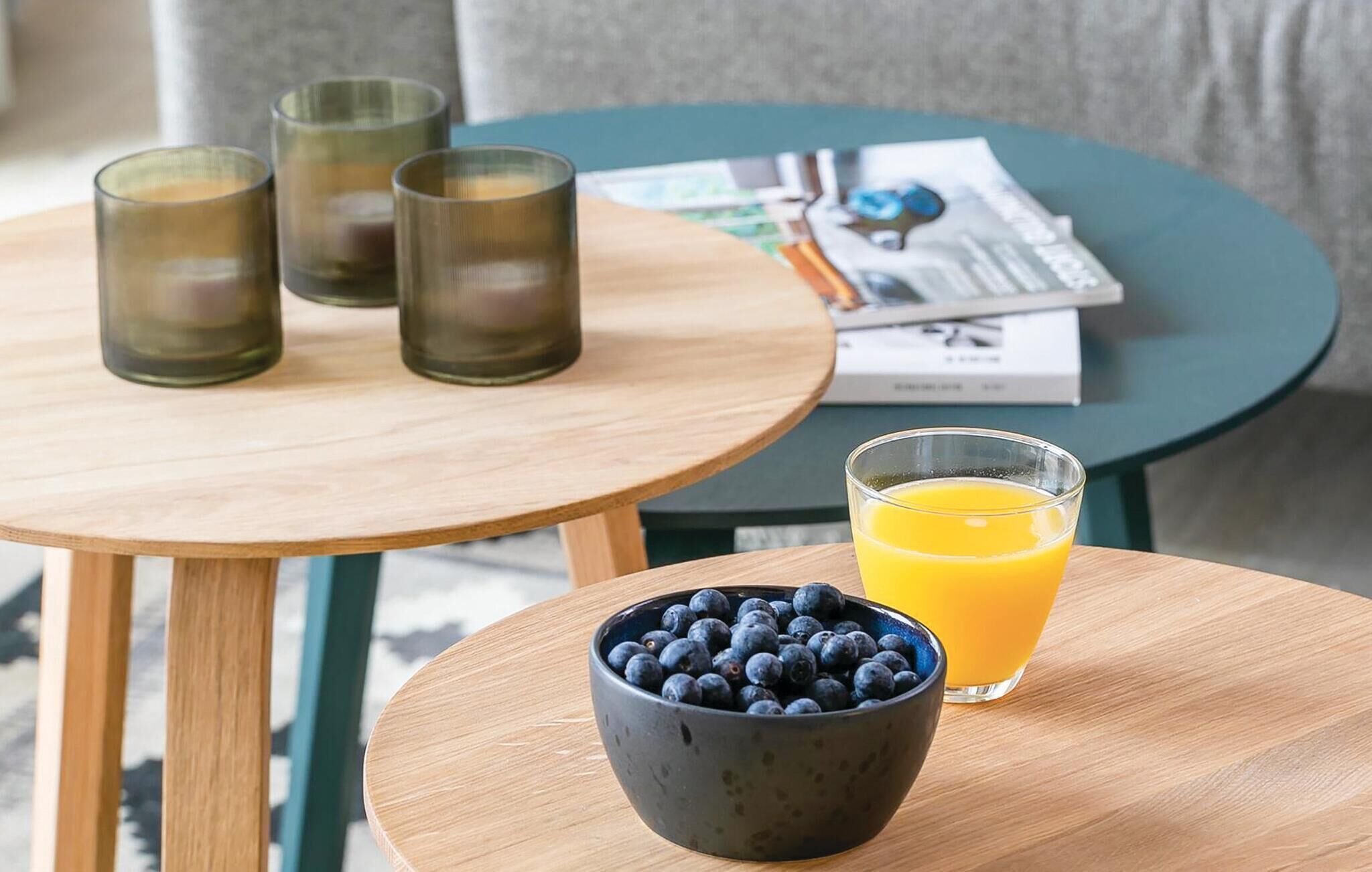 Desayuno con un tazón de arándanos, un vaso de jugo de naranja y tres vasos sobre una mesa de madera.