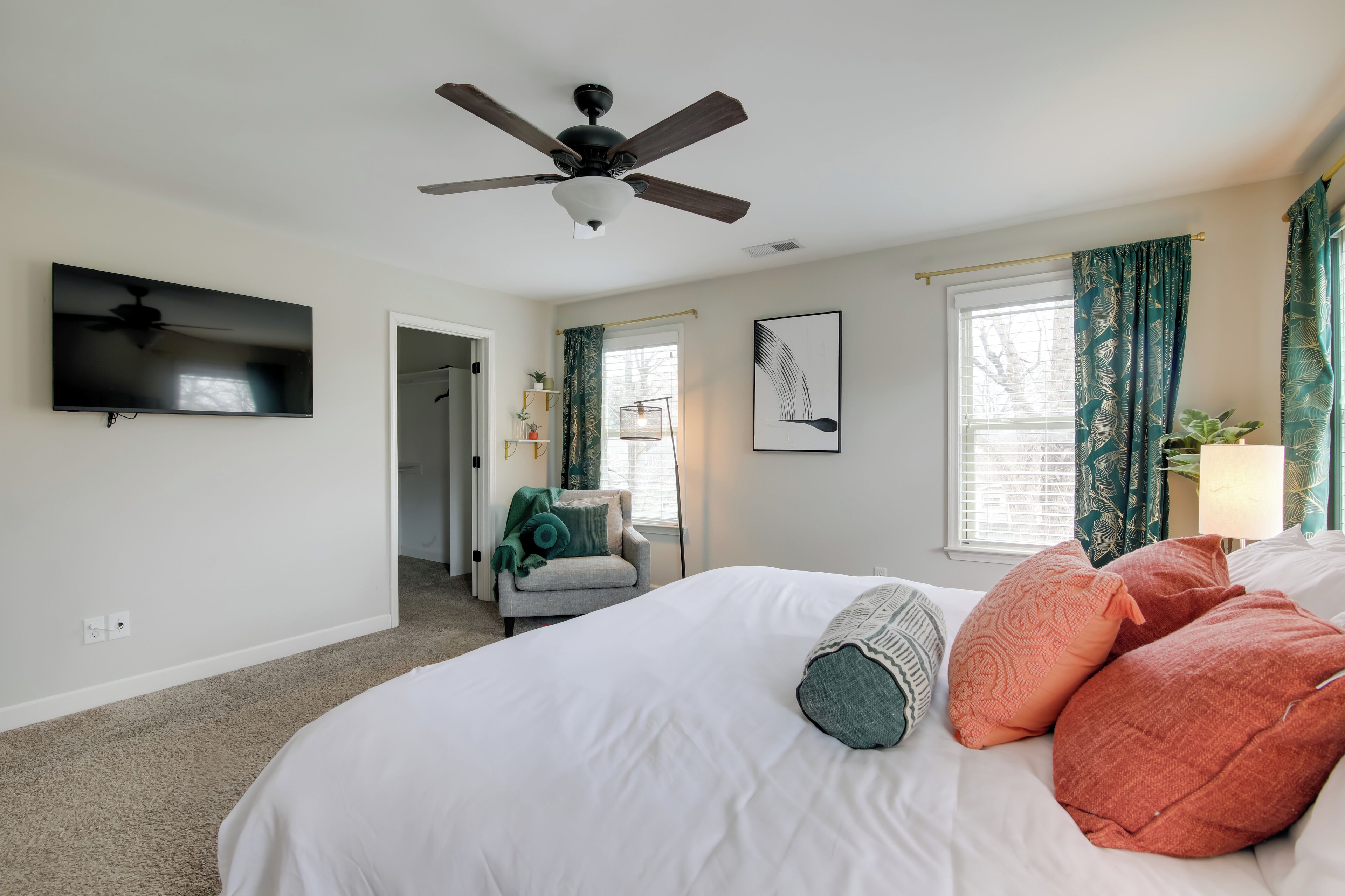 A bedroom with a bed, a ceiling fan, a TV, and a window with curtains.