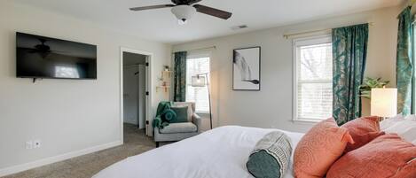 A bedroom with a bed, a ceiling fan, a TV, and a window with curtains.