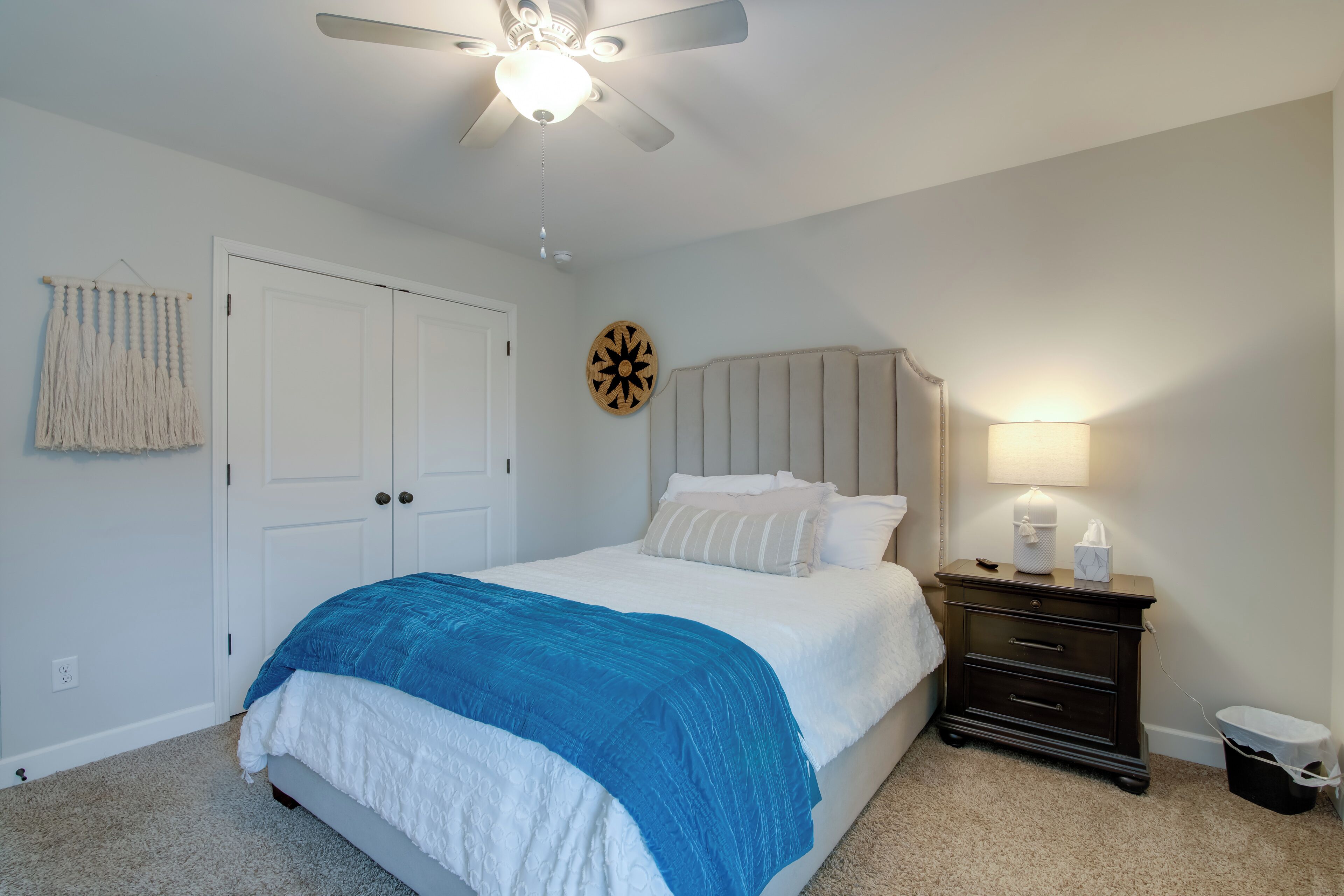 A bedroom with a bed, a nightstand, a lamp, a ceiling fan, and a door.