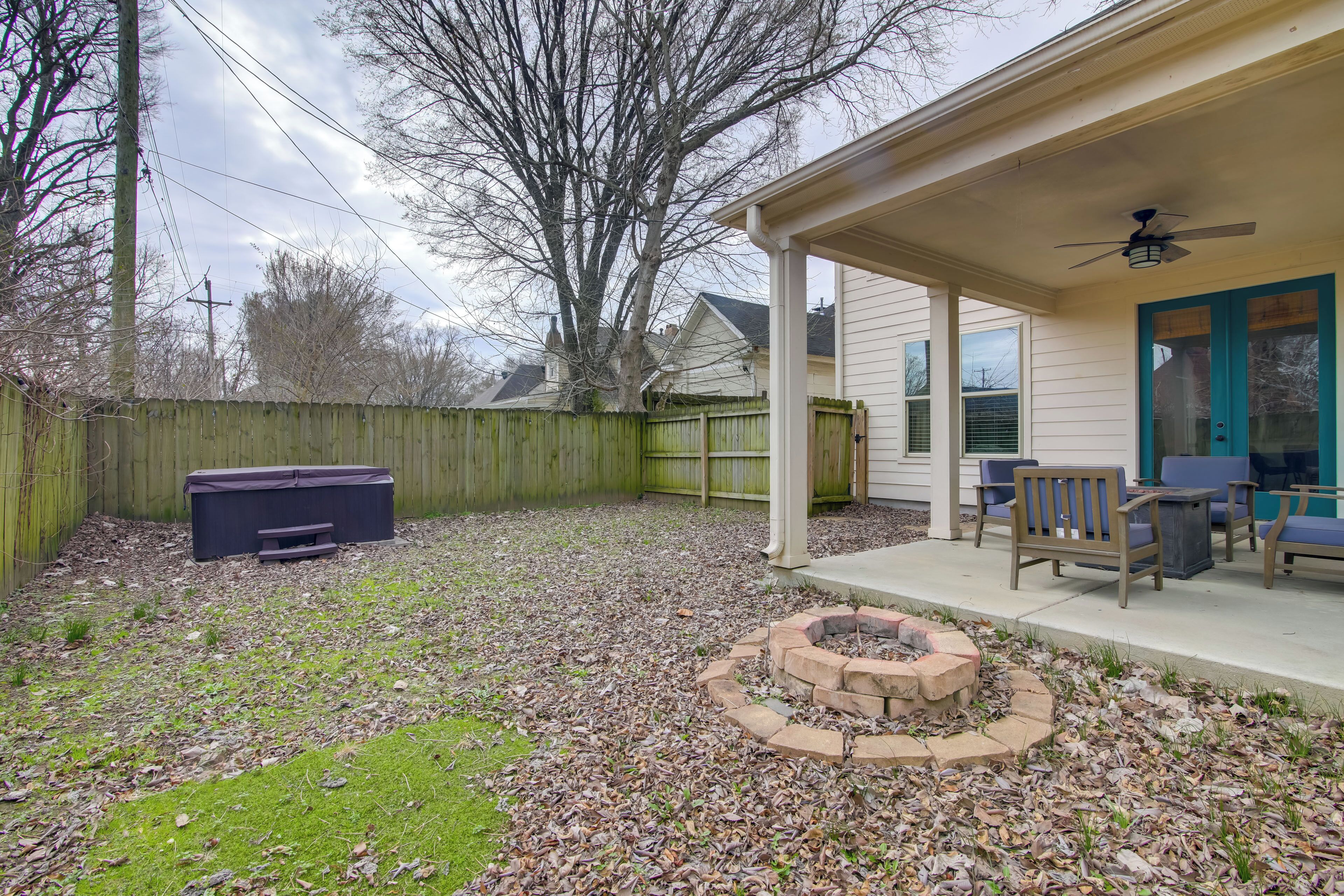 A backyard with a covered patio, outdoor furniture, a fire pit, and a wooden fence.
