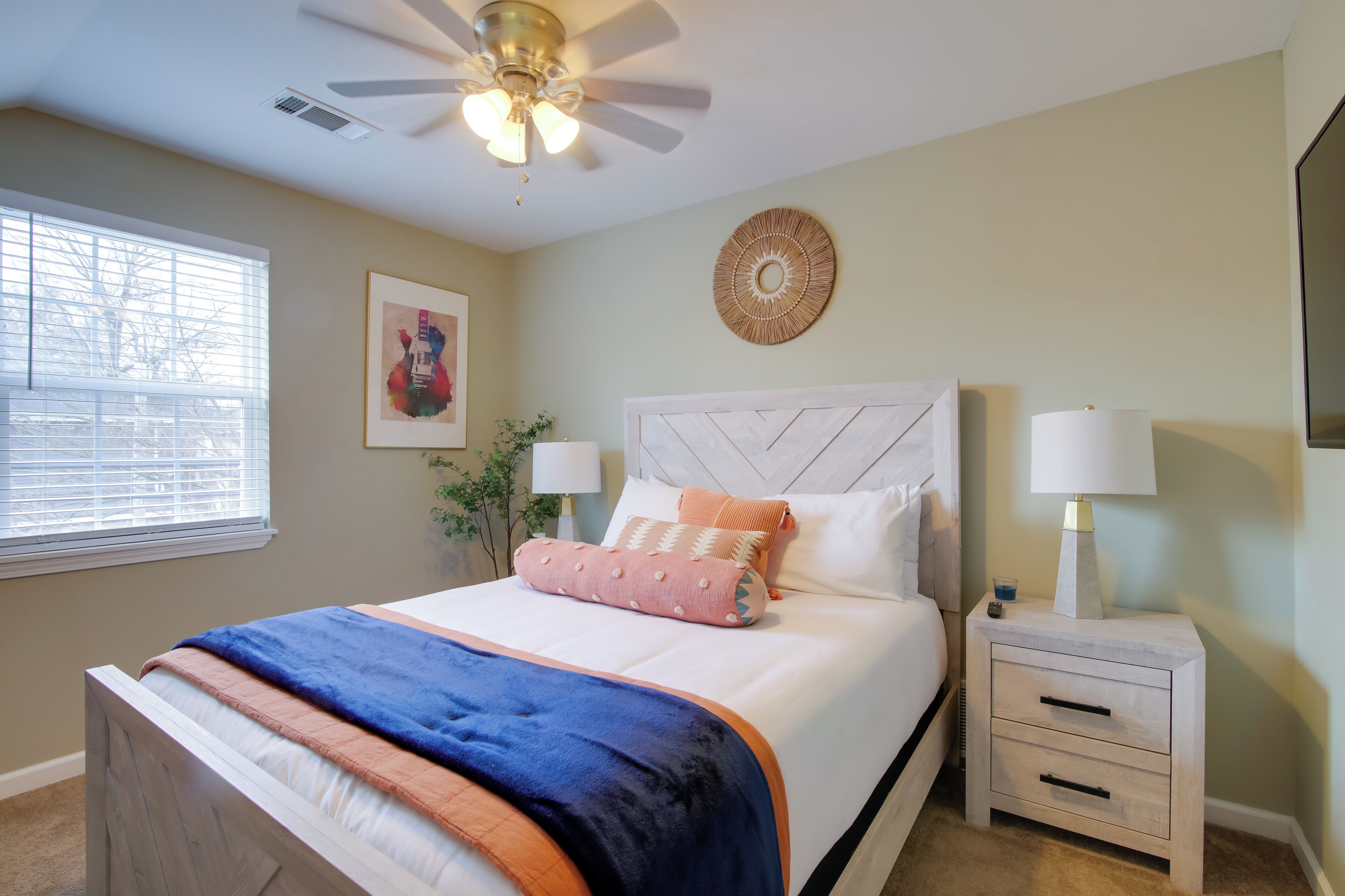 A bedroom with a bed, bedside tables, a ceiling fan, a window, and wall decorations.